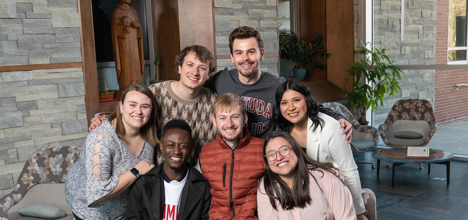Seven Senior Salute students smiling and posed together on a couch in Albertus Magnus Hall of Science